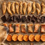 Single-ingredient dog treats — dehydrated chicken, beef liver, salmon skin and sweet potato chews arranged on parchment paper.